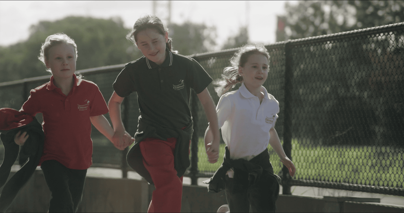 Three young girls running past a fence.